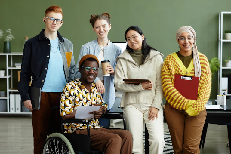 A group of diverse people in an office setting against a green wall.