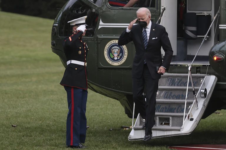 US president, Joe Biden, disembarks from his helicopter, Marine One, and is saluted by a marine soldier.