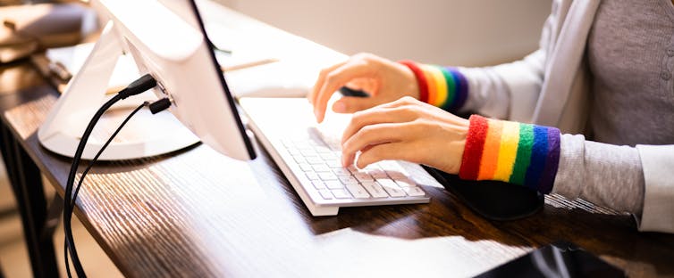 A person wearing LGBTQ rainbow wristbands types on a computer keyboard.