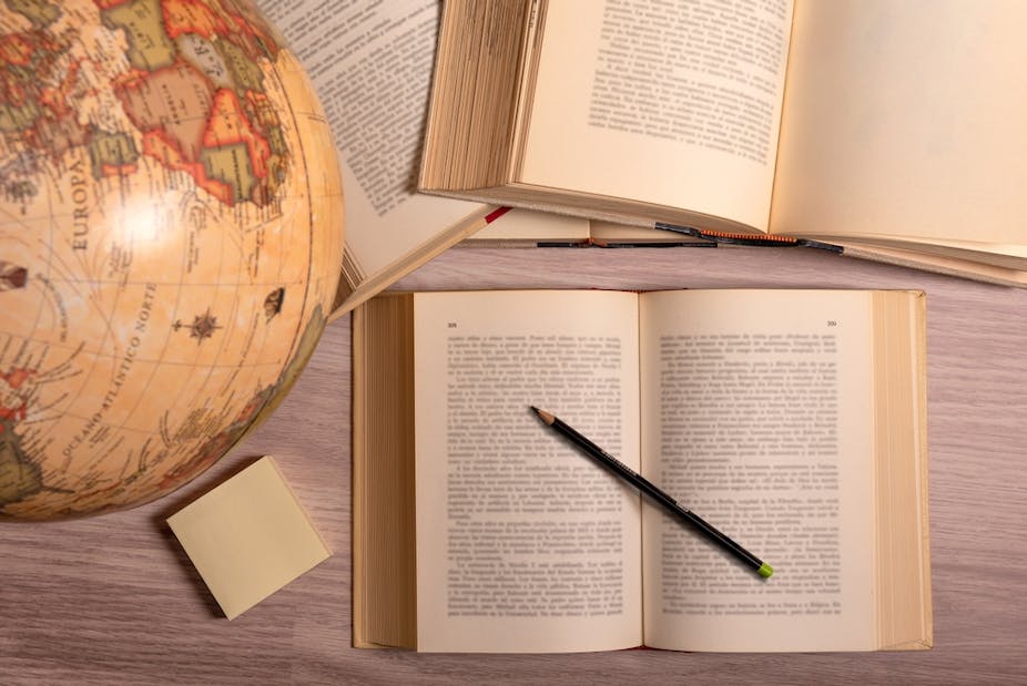Open books, a pencil, sticky notes and world globe on a wooden study table.