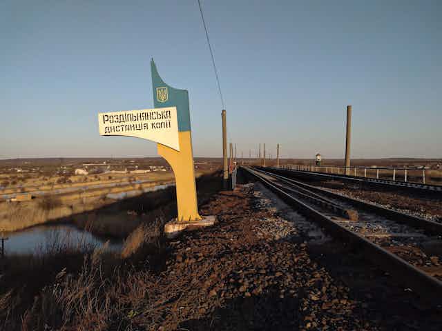 A large Soviet looking sign stands next to an empty railroad track