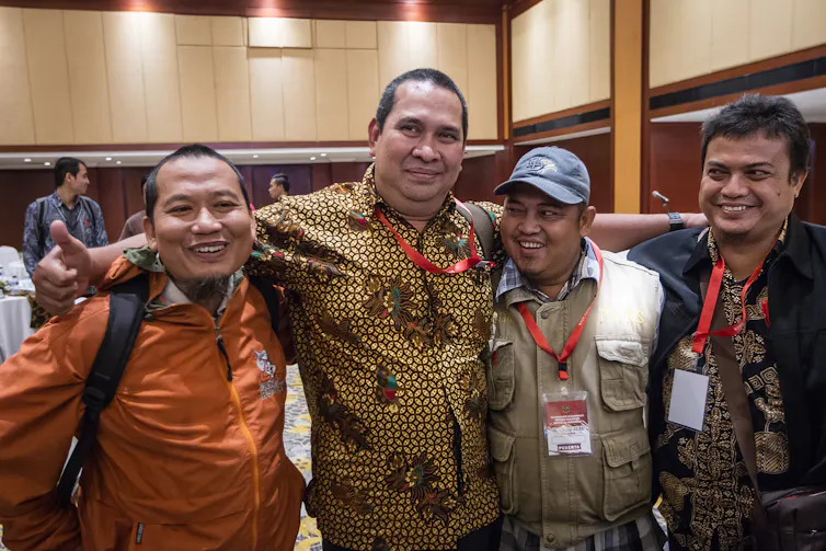 Four Indonesian men pose together and smile broadly, arms around one another