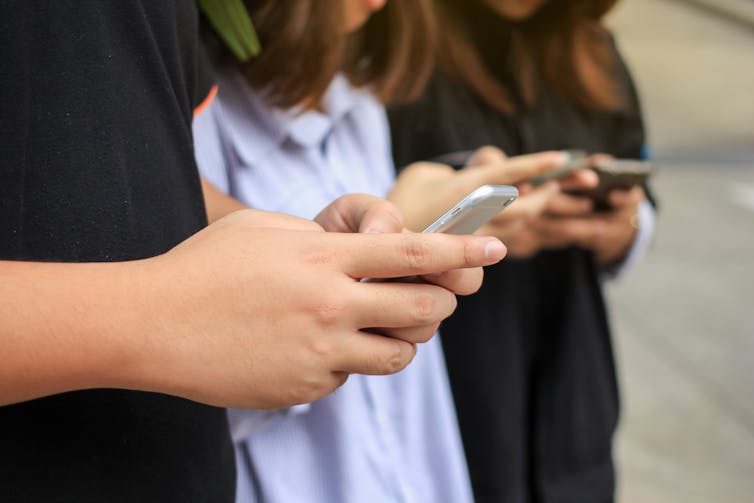 three people in a row with mobile phones in their hands