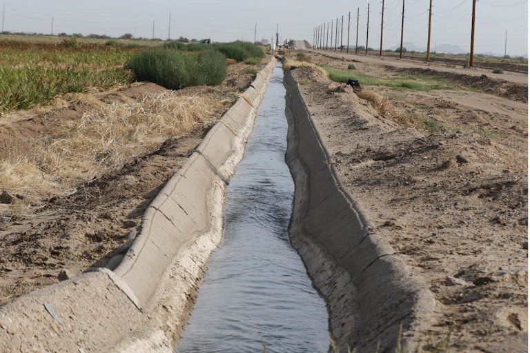 Water in a narrow concrete-sided canal between a field and a road