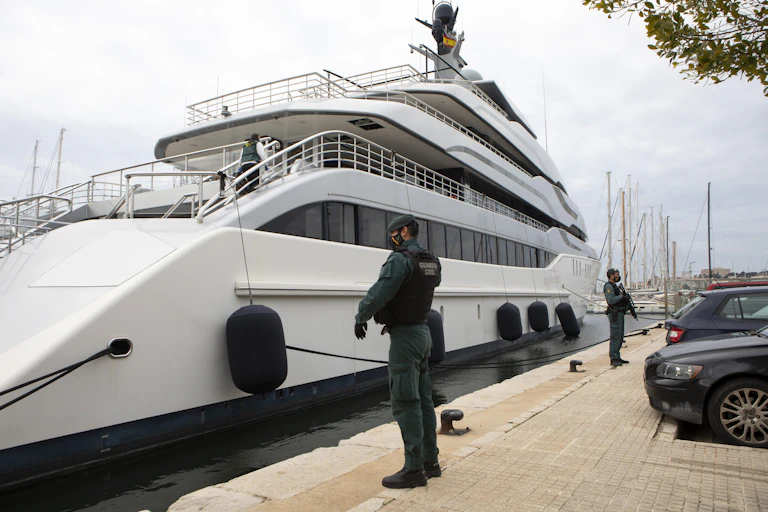 A large white yacht is docked by a dock in Spain as two armed civil guards stand watch