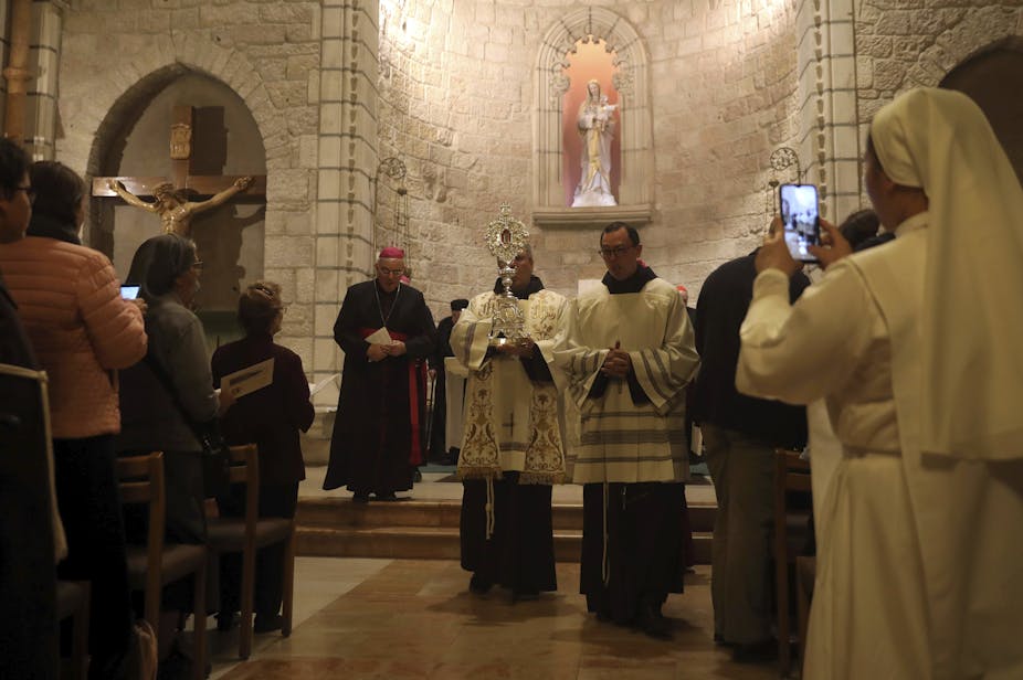 Two priests holding a relic in the Notre Dame Church in Jerusalem, as people look on.