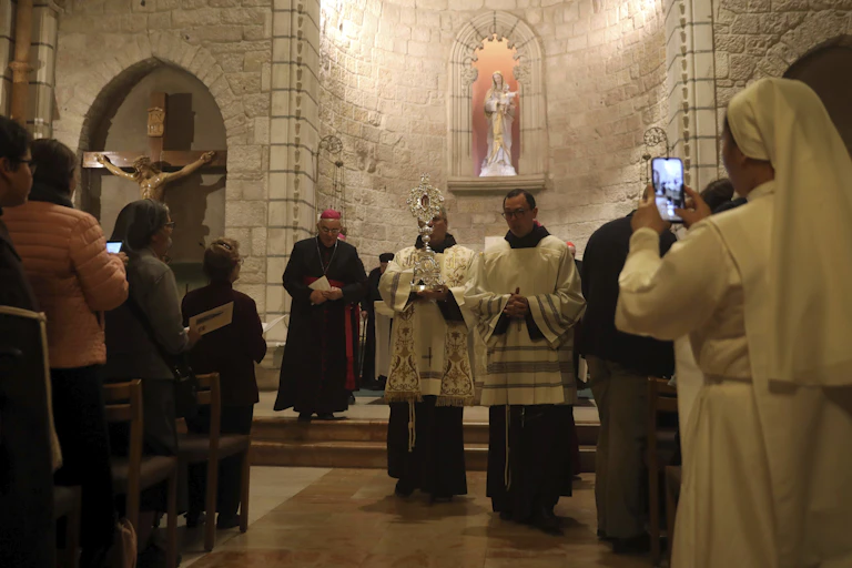 Two priests holding a relic in the Notre Dame Church in Jerusalem, as people look on.