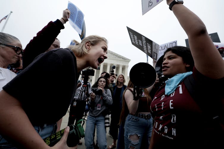 A woman is seen shouting in the face of a protester holding up a placard.