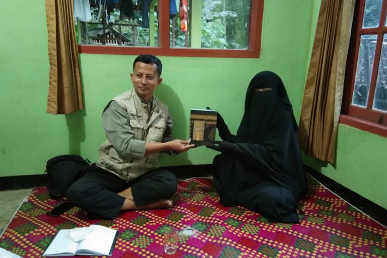 A man wearing a vest sits next to a woman covered in a full burqa