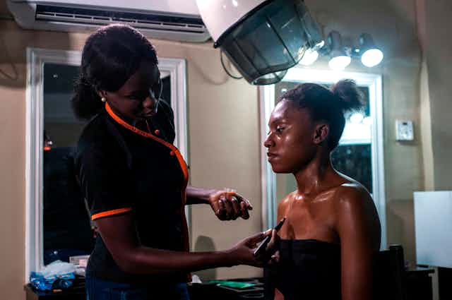 A beautician applies a skin toning treatment on a dark-skinned woman at a beauty salon.