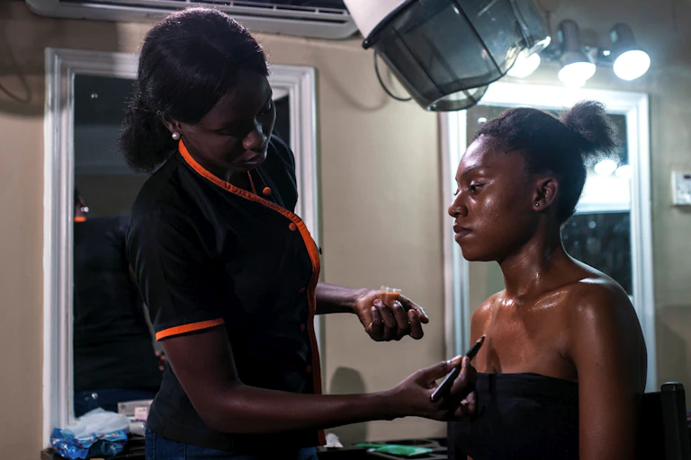 A beautician applies a skin toning treatment on a dark-skinned woman at a beauty salon.