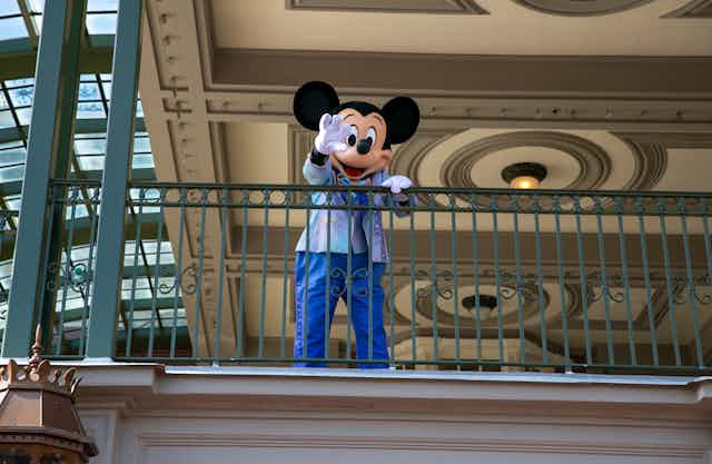 A person in a mickey mouse costume waves from a balcony 