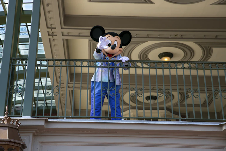 A person in a mickey mouse costume waves from a balcony