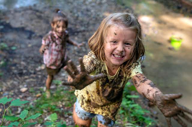 Two young girls who have been playing the mud run toward the camera with muddy hands, smiling