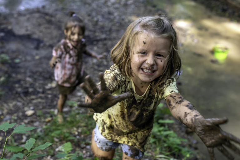 Two young girls who have been playing the mud run toward the camera with muddy hands, smiling