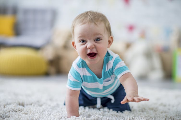 A grinning baby boy crawls toward the camera through thick white carpet.