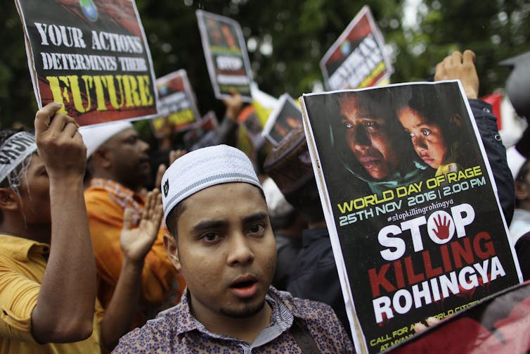 a young man in a kufi holding a placard reading STOP KILLING ROHINGYA