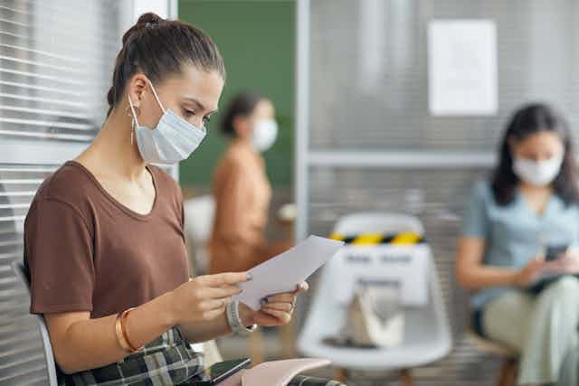 Woman wearing mask reading letter in clinic waiting room