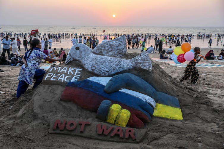 A beach scultpure of Russian and Ukrainian handshake with a dove and sign saying 'make peace'.