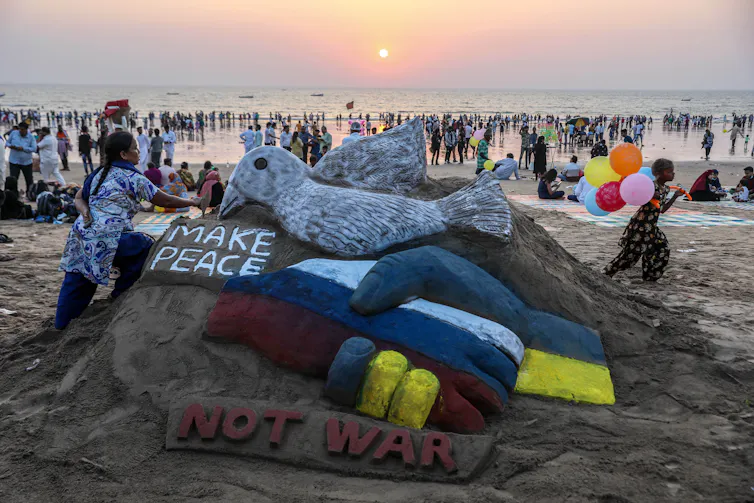 A beach scultpure of Russian and Ukrainian handshake with a dove and sign saying 'make peace'.