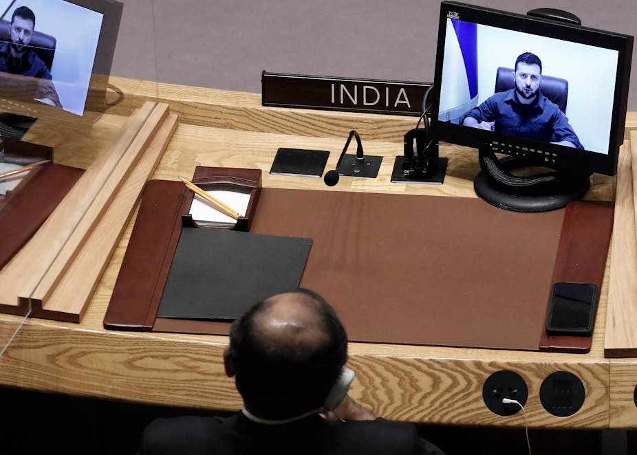 India's UN representative watches Volodmyr Zelensky on a TV screen. 