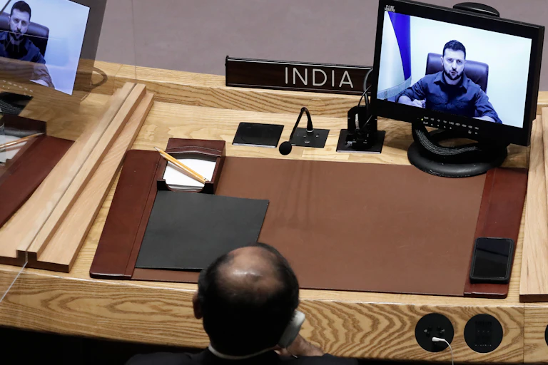 India's UN representative watches Volodmyr Zelensky on a TV screen.