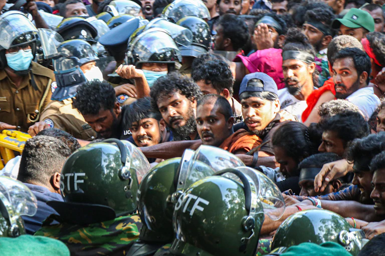 Police and security forces in green helmets hold back the protesting crowds.