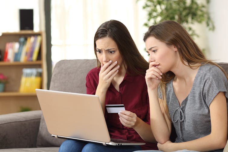 two women appear shocked as they look at a laptop screen