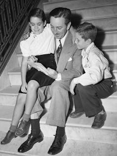 Man sits on steps drawing for two kids.