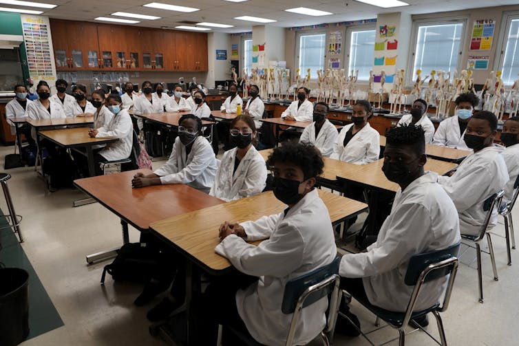 A group of young Black people sit around tables in a classroom