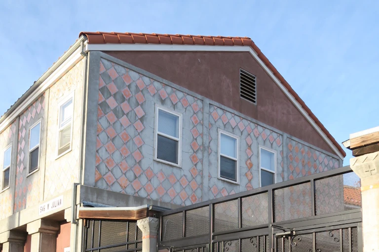 A coral or terracotta-looking roof is seen atop walls featuring pink and grey squares