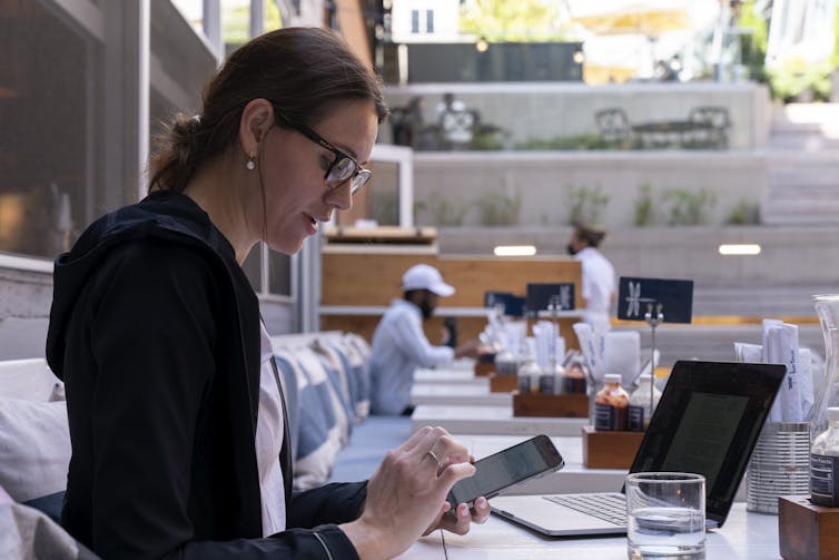 Woman sitting at an outdoor restaurant table using a cell phone