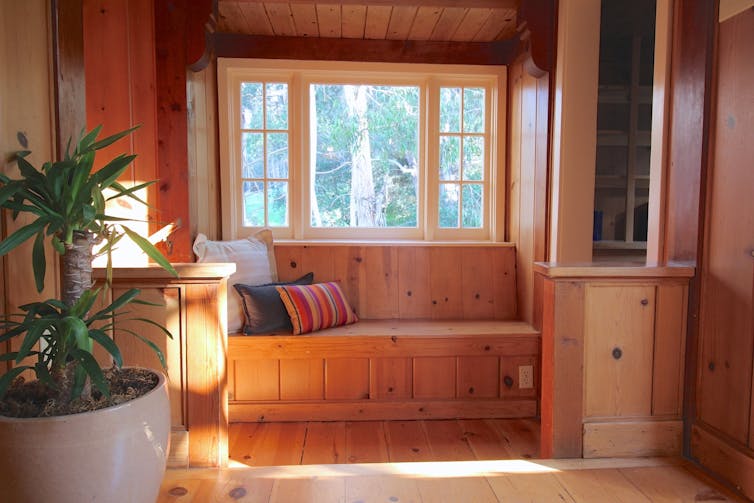 View of a home's hallway, showing wood walls and a built-in bench under a large window facing onto trees.