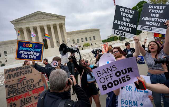 Protestors hold signs like 'divest from big abortion now' and 'LGBT Democrat standing for life' and 'Bans off our bodies' outside the US Supreme Court