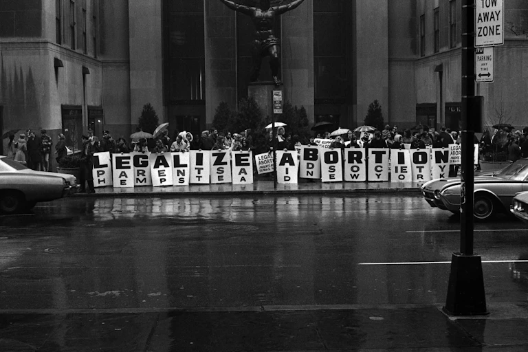A group of people standing in a line in front of a huge city building, holding signs that say 'LEGALIZE ABORTION.'