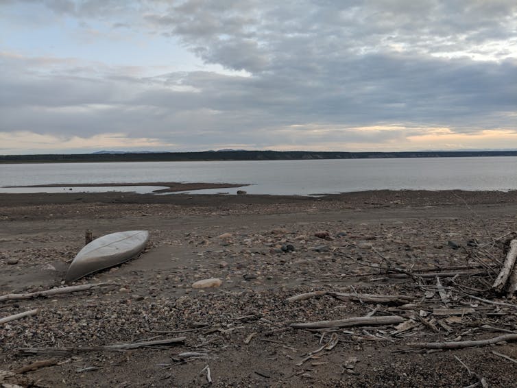 A canoe on a rocky beach with water in the background