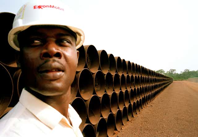 A worker in an oil company hard hat stands in front of pipes for a pipeline in Cameroon.