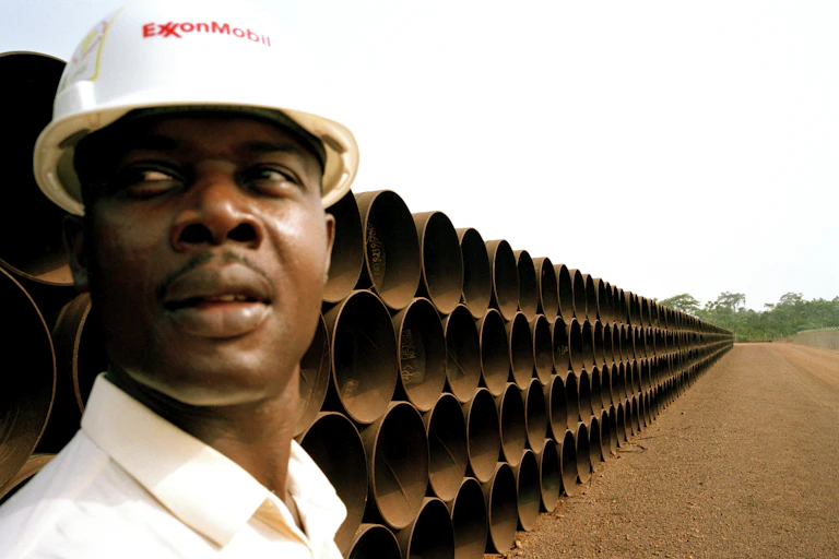 A worker in an oil company hard hat stands in front of pipes for a pipeline in Cameroon.