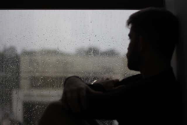 Man looks out a window on a grey, rainy day
