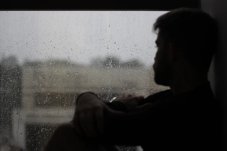 Man looks out a window on a grey, rainy day