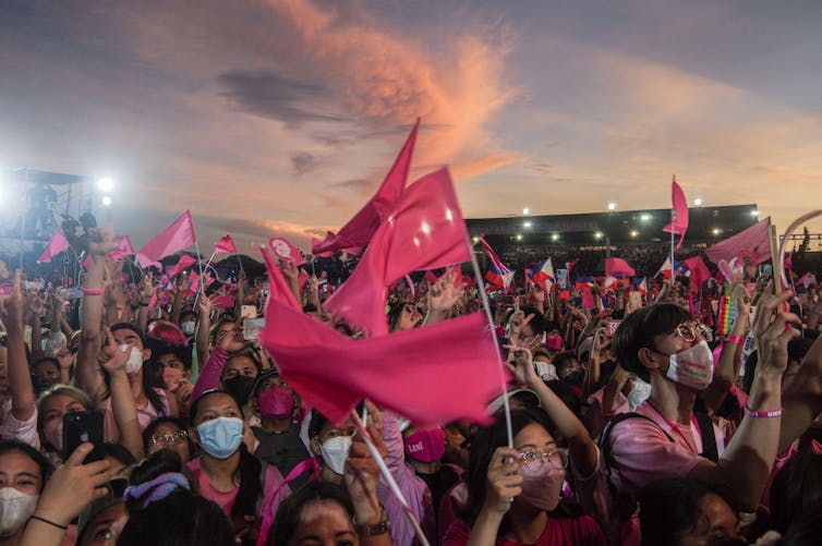 Uma multidão carregando bandeiras cor de rosa.