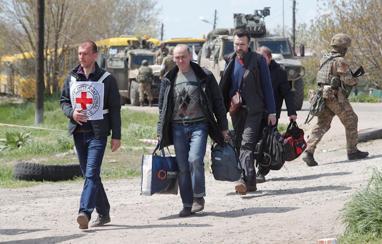 A member of the International Red Cross escorts Ukrainian civilians carrying luggage.