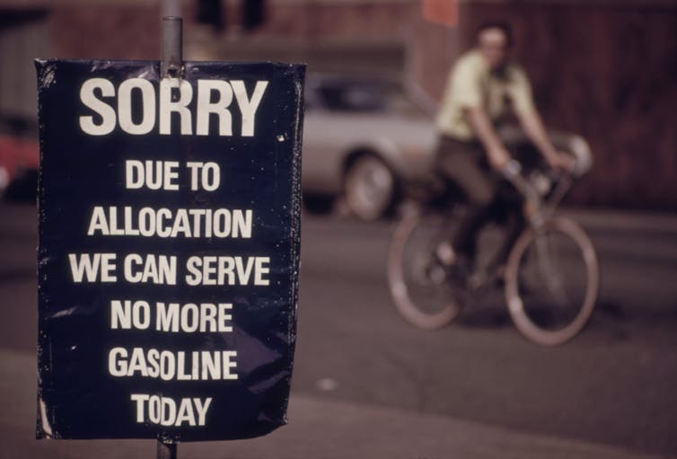 A sign announces no more gasoline sales while a man cycles in the background.