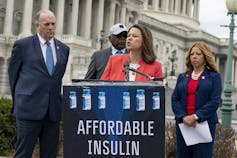 Two women and two men in suits next to an'affordable insulin' sign in front of the U.S. Capitol building.