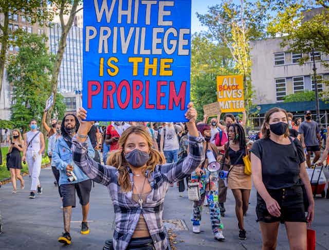 A white protester is seen holding a sign that reads 'White Privilege Is The Problem.'