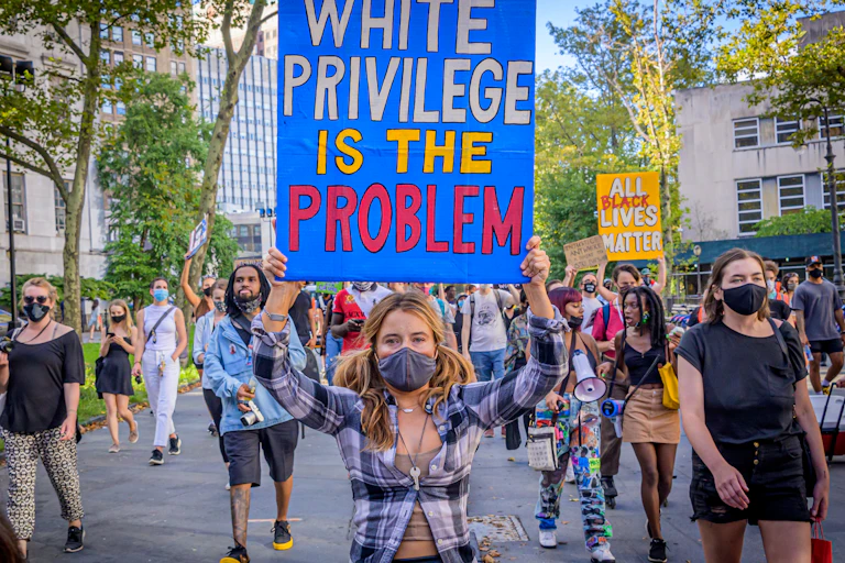 A white protester is seen holding a sign that reads 'White Privilege Is The Problem.'