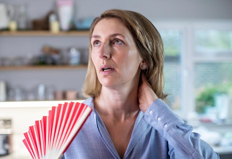 Woman experiencing a hot flush uses a paper fan to cool down.