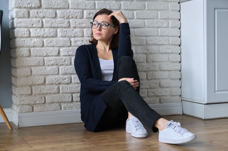 Woman sitting against a wall looking uncomfortable