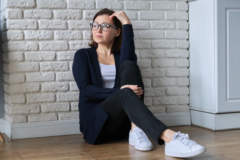 Woman sitting against a wall looking uncomfortable
