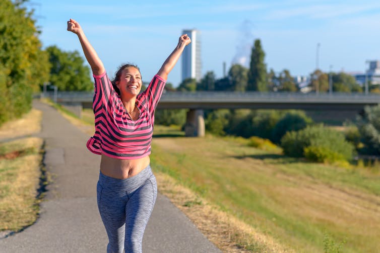 A woman in fitness clothes running with her arms in the air